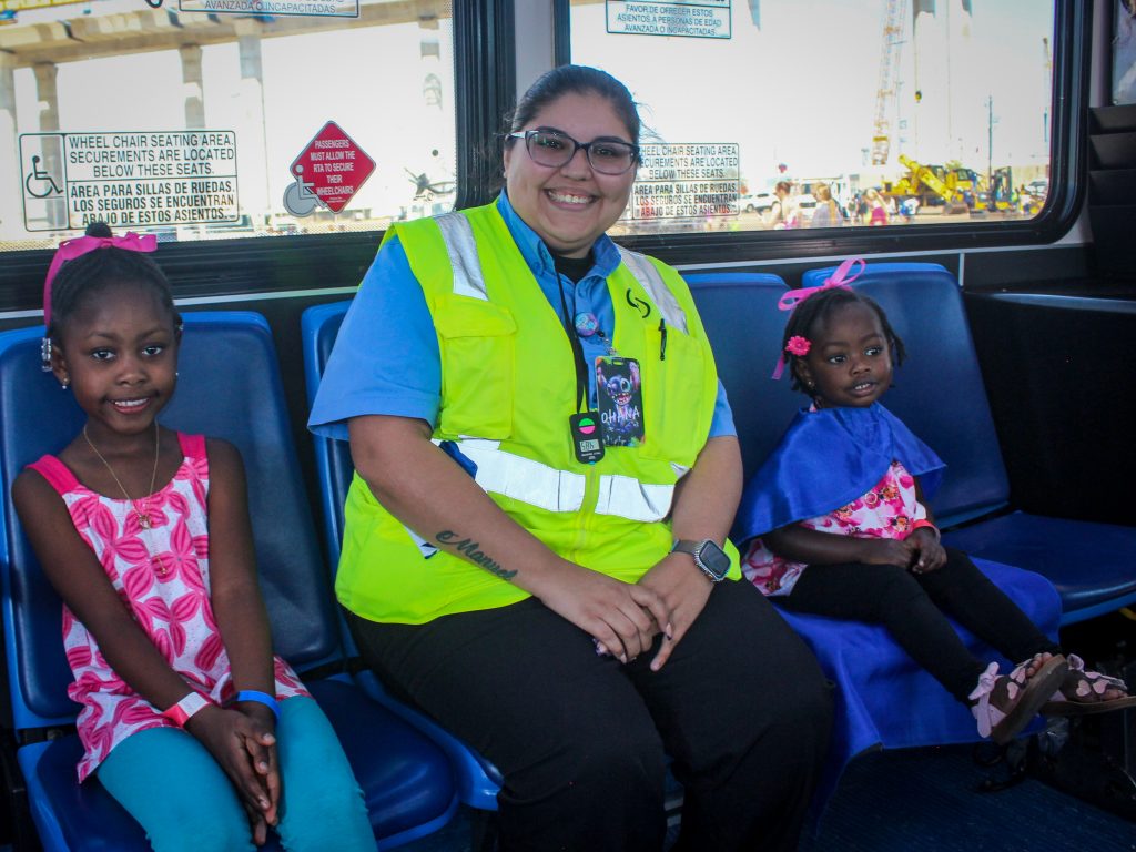 A young child sits on either side of a safety officer on a bank of bus seats.