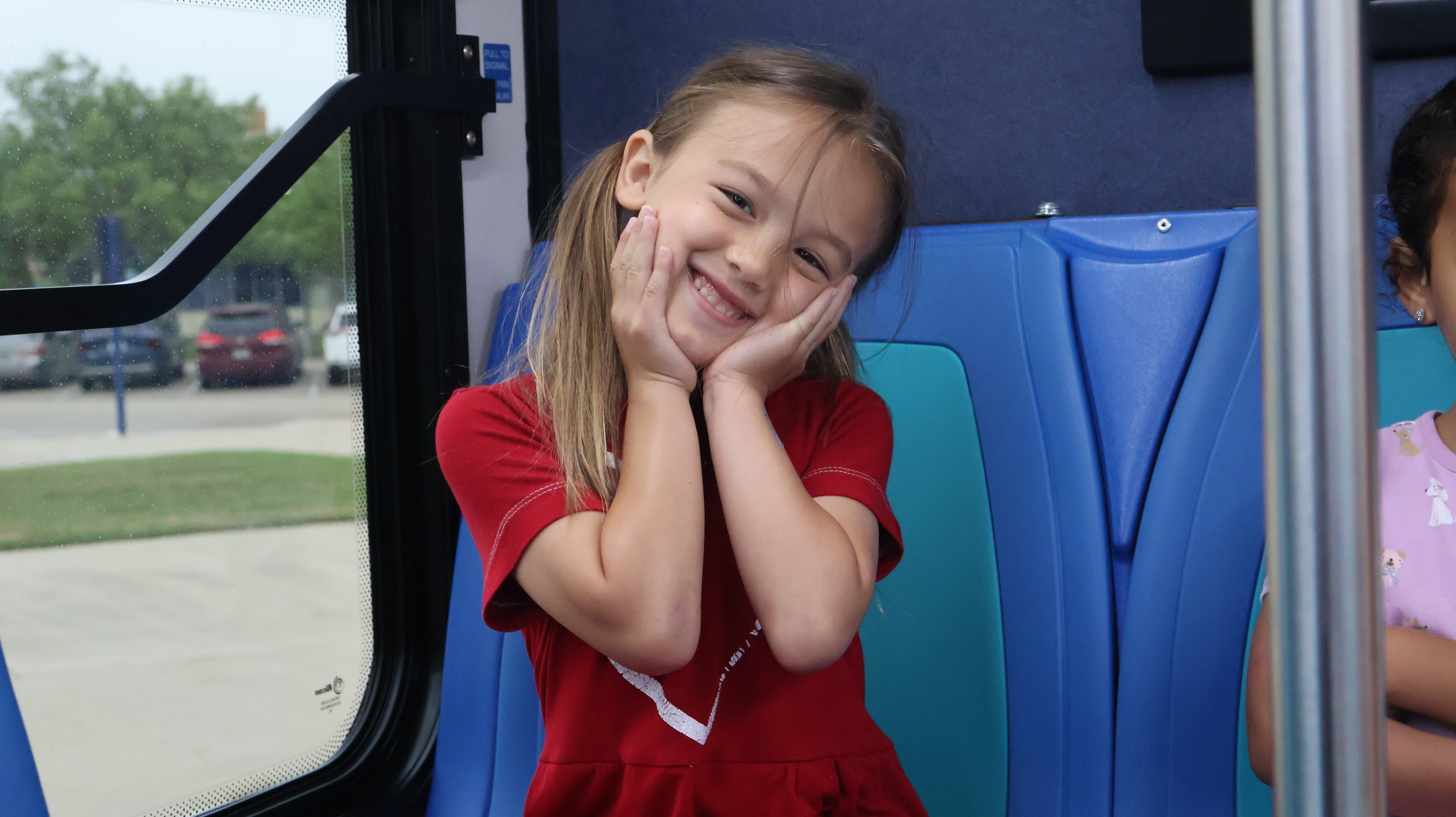 A young child on a bus seat smiles for the camera.
