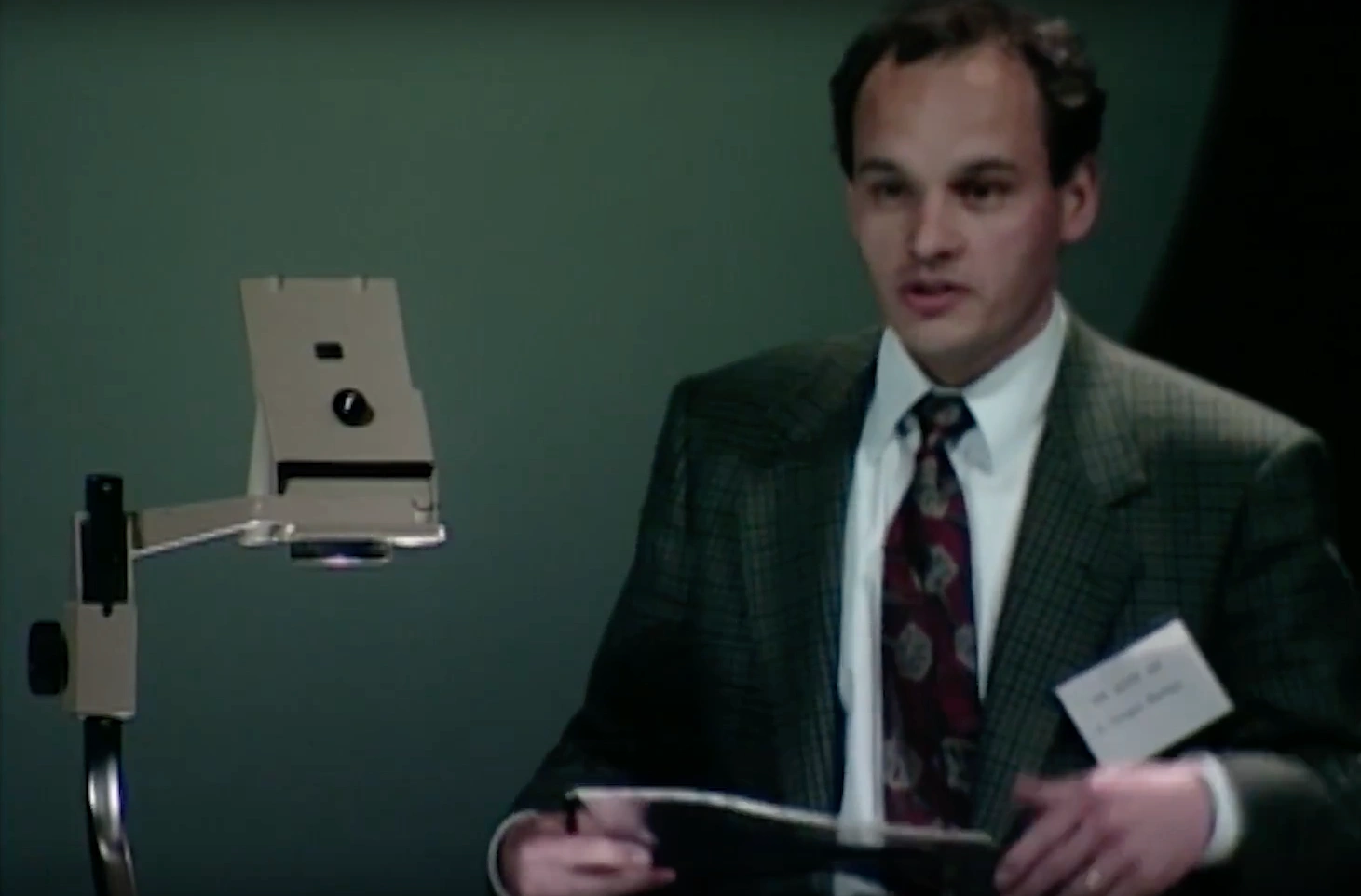 L. Gregor Herten standing beside an optical microscope, green walls in the background.