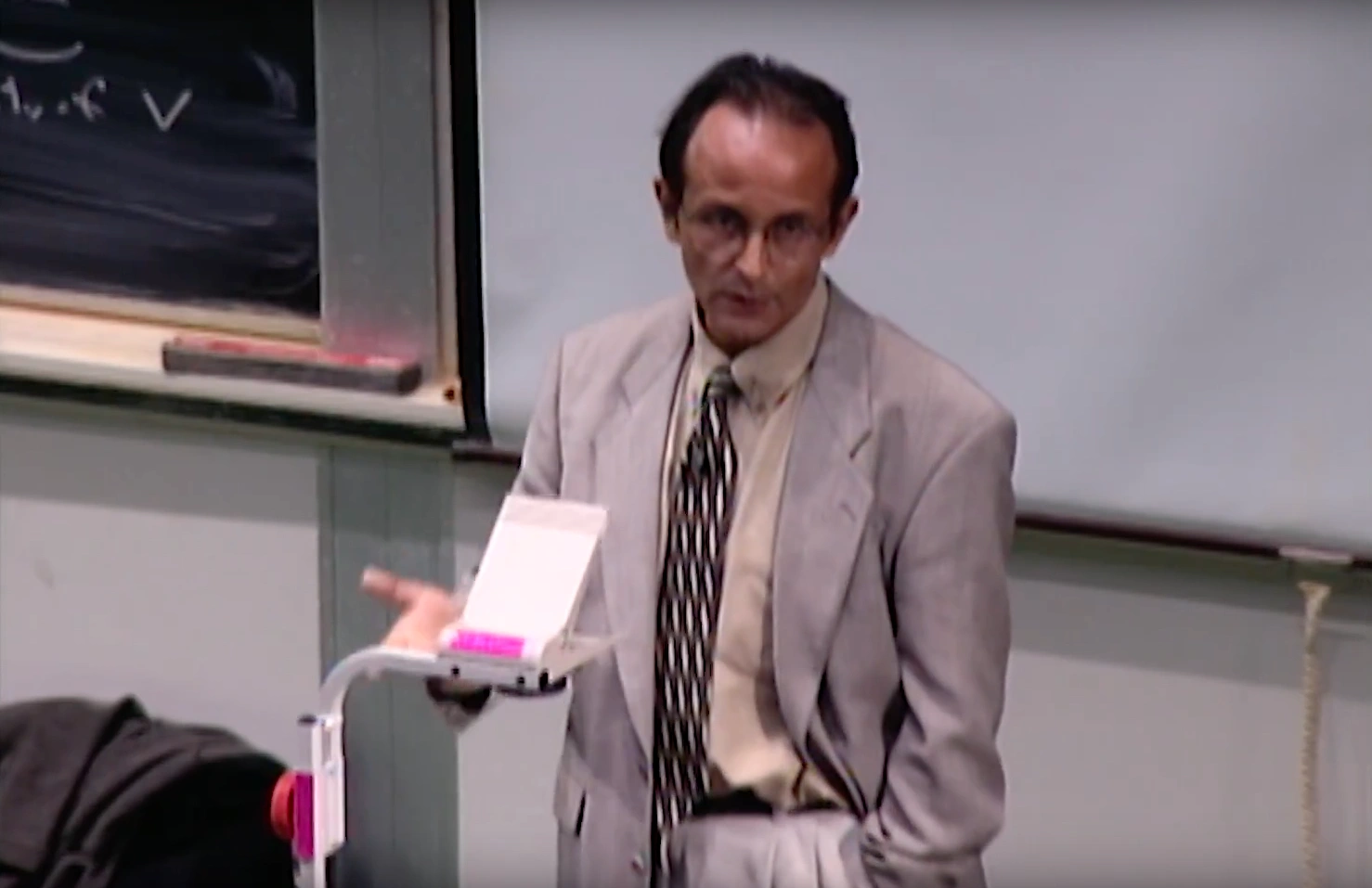 Francisco Varela lecturing in a classroom, projector screen and chalkboard in the background