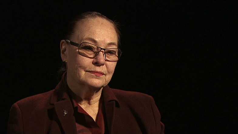 Brit J. d'Arbeloff seated in front of a black background for an on camera interview.