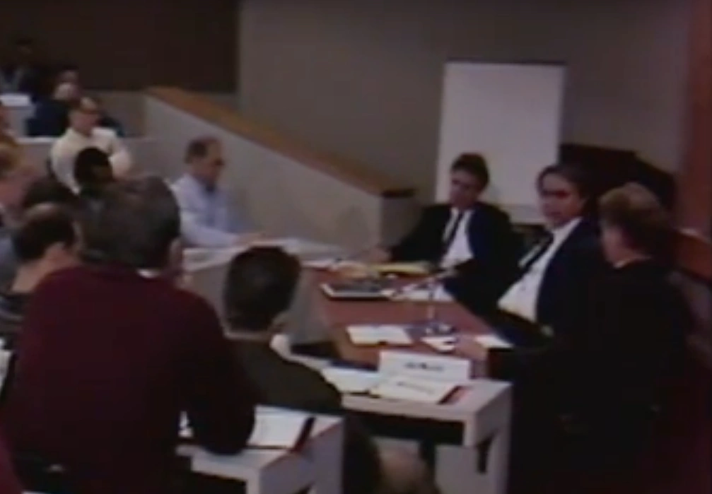 Group of men surrounding a table in a classroom and looking ahead at a man with a flipchart
