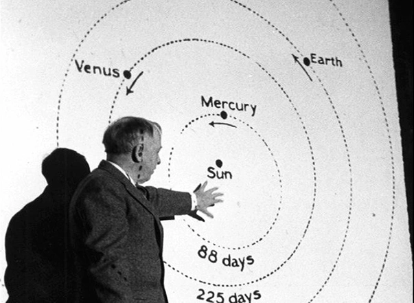 A professor stands at a chart with concentric circles.