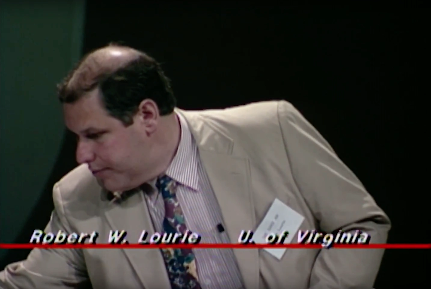 Robert Lourie, standing on stage, reaching downward. Dimly lit green wall in background.