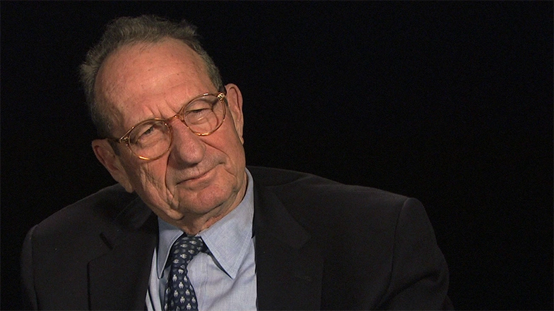 John M. Deutch seated in front of a black background for an on camera interview.