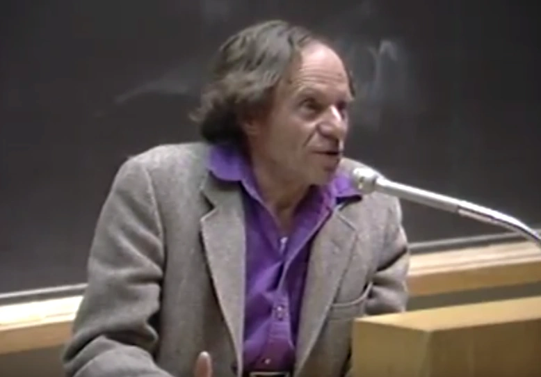 Philip Morrison speaking at a podium in front of a chalkboard