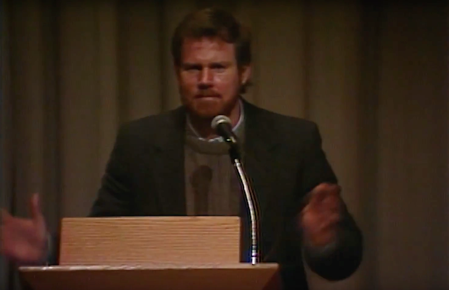 Michael Urban standing at podium on stage, in front of a cream curtain