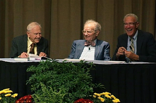 Franco Modigliani, Robert M. Solow, and Paul Samuelson sitting behind a table and smiling together, cream curtain in background