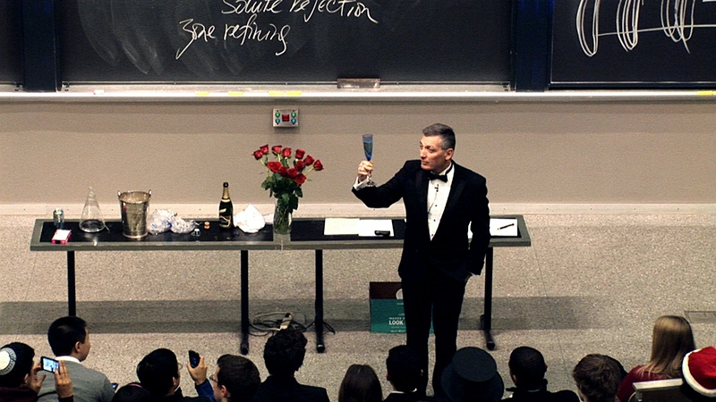 Donald R. Sadoway makes a champagne toast to a classroom, chalkboards in background