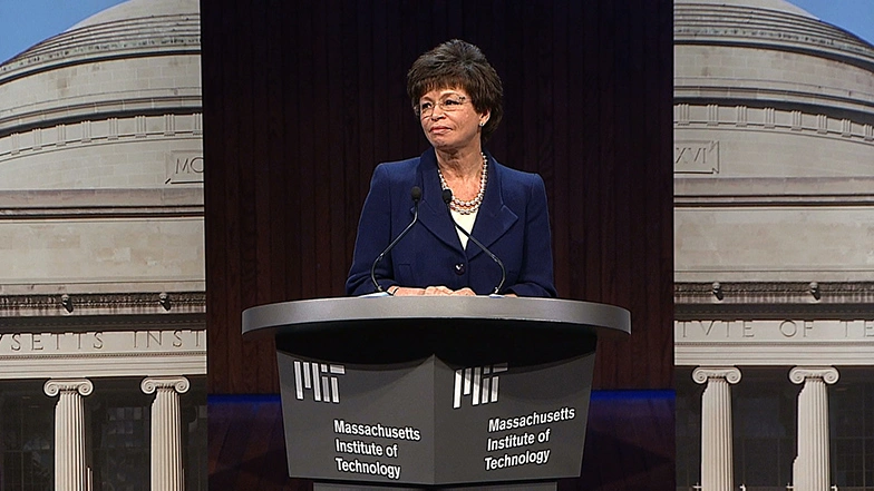 Valerie Jarrett speaks at a podium, a large image of MIT's great dome building in the background
