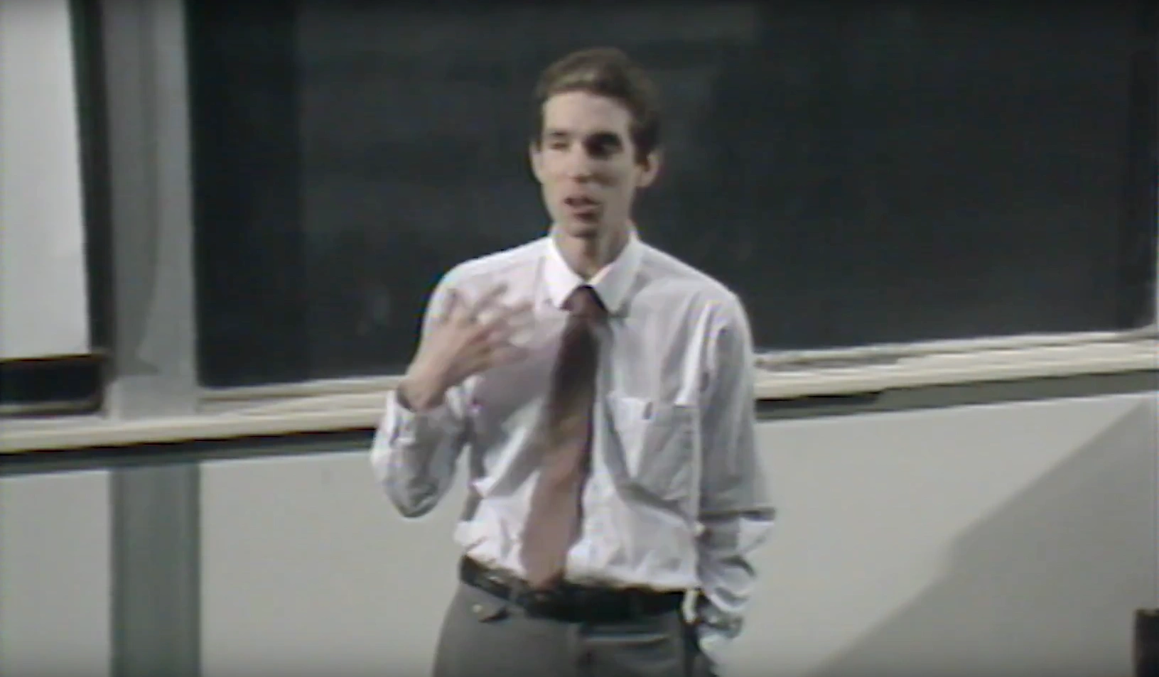 A man delivers a lecture in a classroom for Project Athena - X Windows Conference, chalkboard in the background