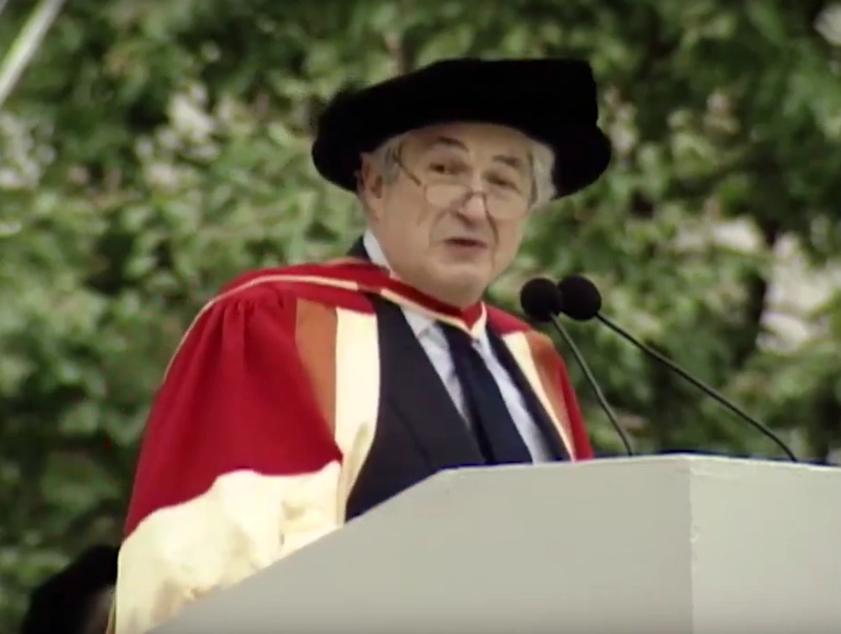 James D. Wolfensohn, wearing commencement attire, speaking at podium on outdoor stage, trees in background