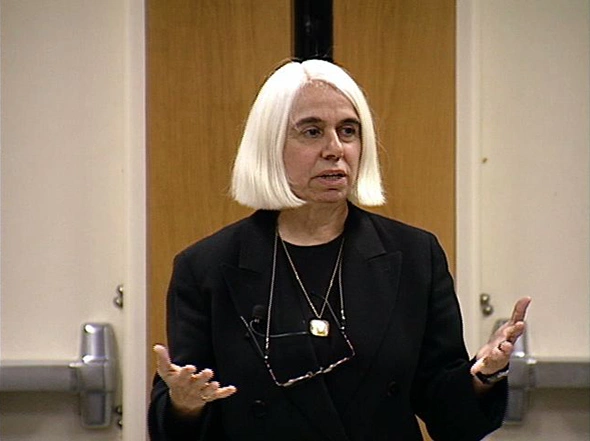 Virginia Valian delivering a lecture in a classroom, gesturing with her hands as she speaks.
