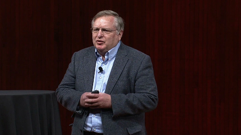Patrick H. Winston speaks on stage, black backdrop in background