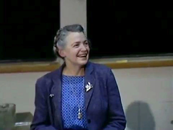 Mildred Dresselhaus stands in front of a chalkboard, looking to the side and smiling.