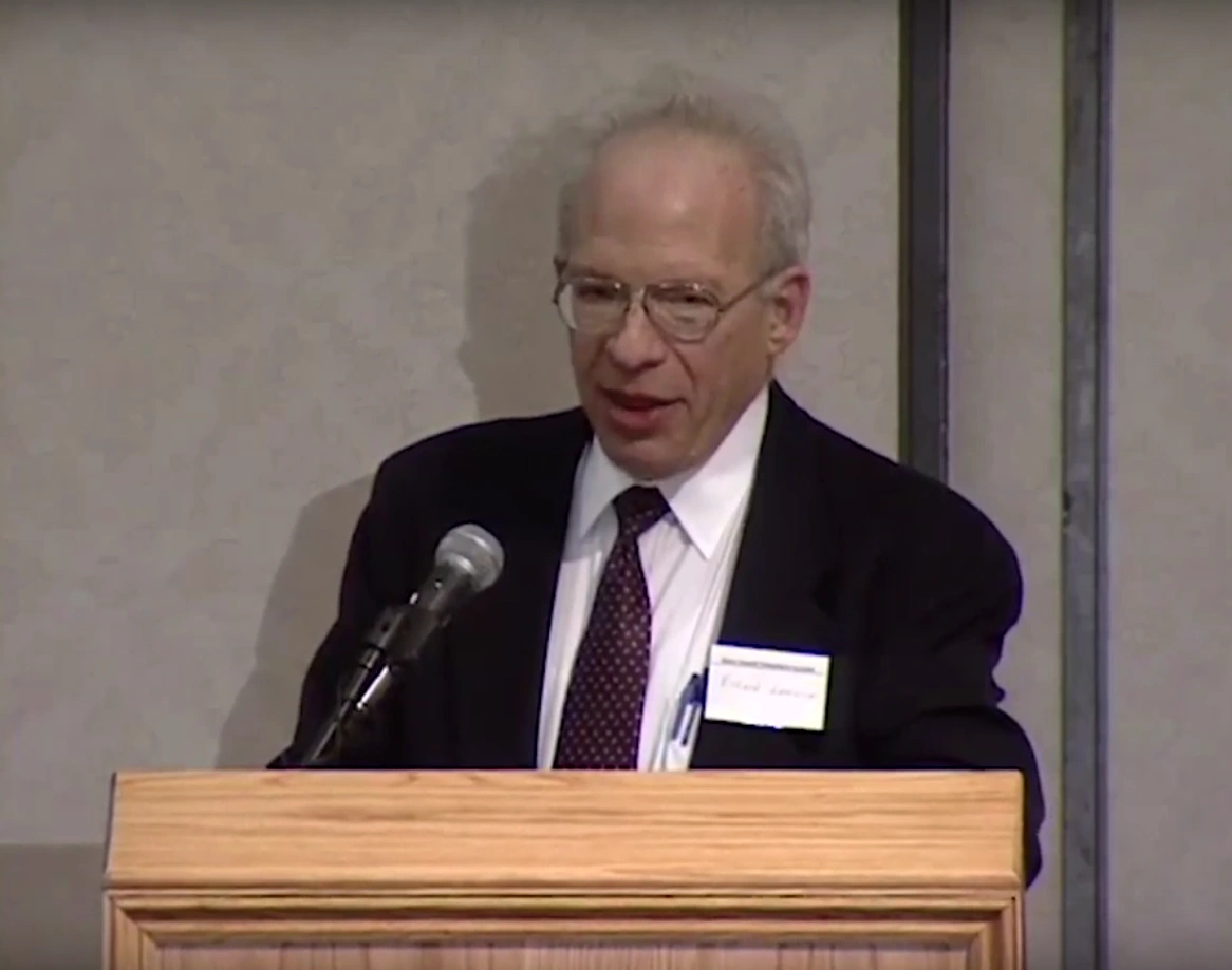 Richard Garwin speaking at a podium, cream colored wall in background