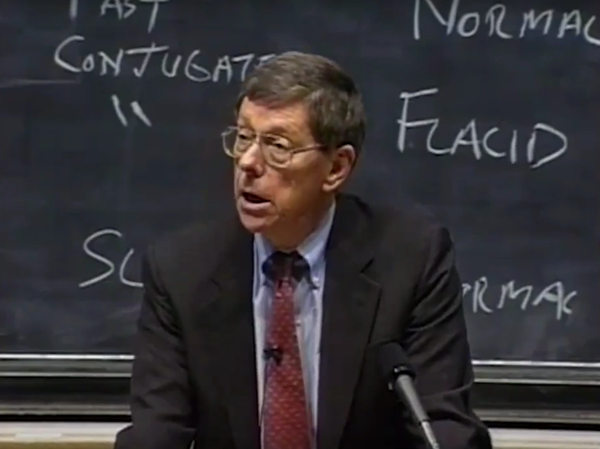 John A. Armstrong lecturing at a podium in a classroom, chalkboard in the background.