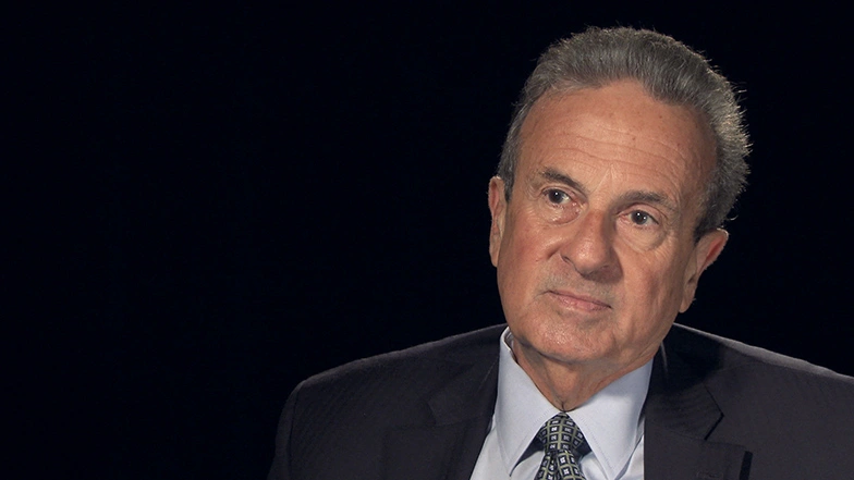 Richard Rossi seated in front of a black background for an on camera interview.