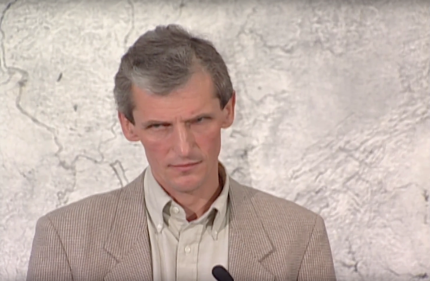 Wolfgang Ketterle standing at a podium in front of a marble wall, looking to the side,