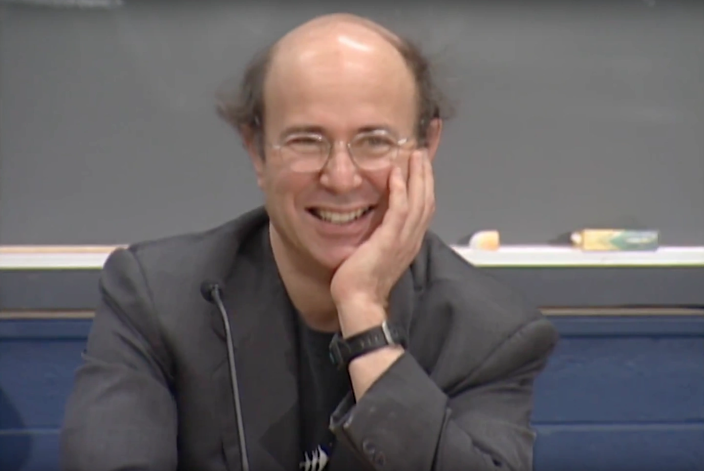 Frank Wilczek stands at podium in classroom, resting his head in one hand and smiling