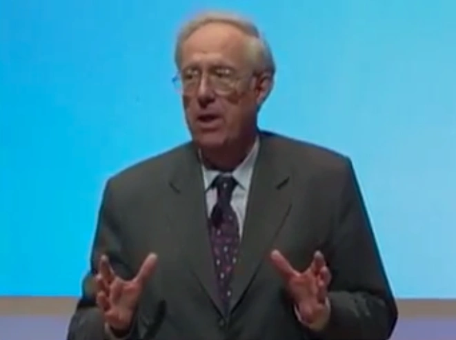 Michael Dertouzos speaking on stage  in front of blue background