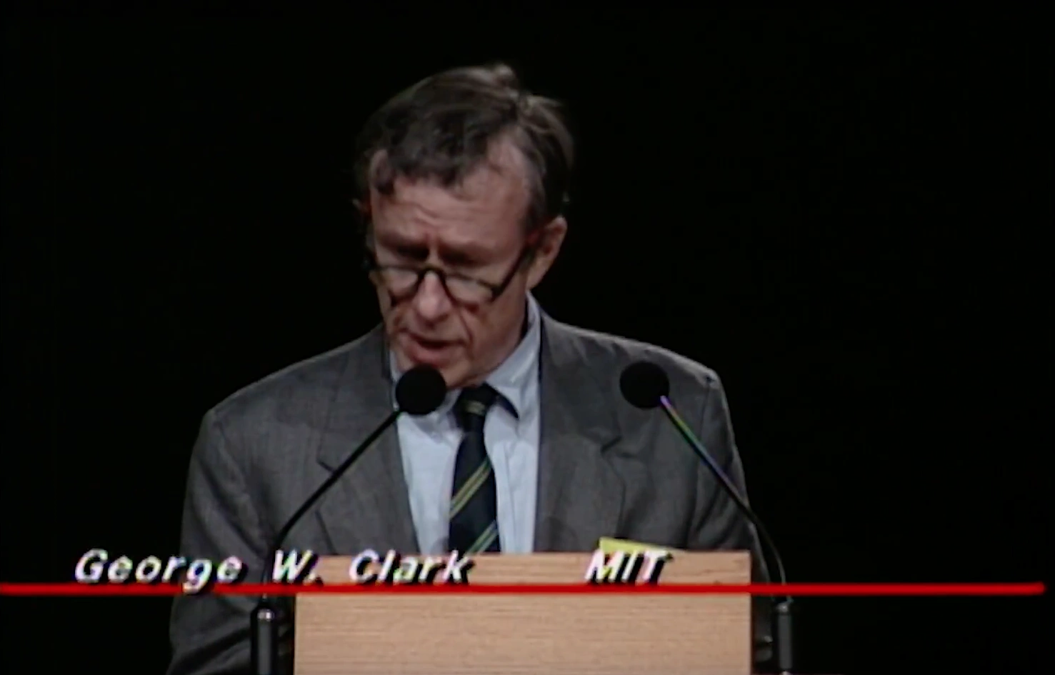 George W. Clark speaking at a podium on stage, in front of a dark background
