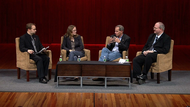 A panel of four speakers seated in chairs on a stage discussing the future of exploration.