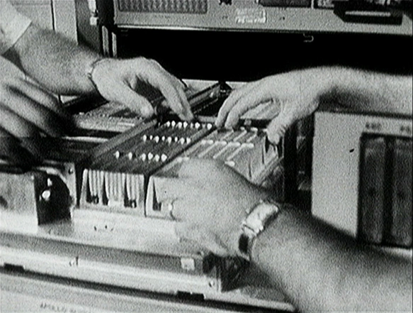 Two sets of hands operating the computer brought aboard Apollo. Black and white photo.
