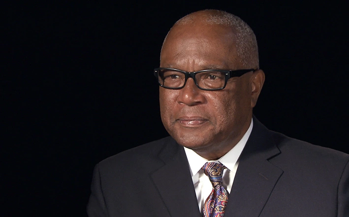 Kenneth Reeves seated in front of a black background for an on camera interview, staring ahead.