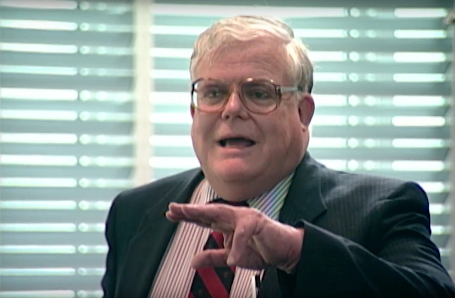 John H. Sununu speaking passionately, gesturing with hand for emphasis, daylight coming through blinds in background