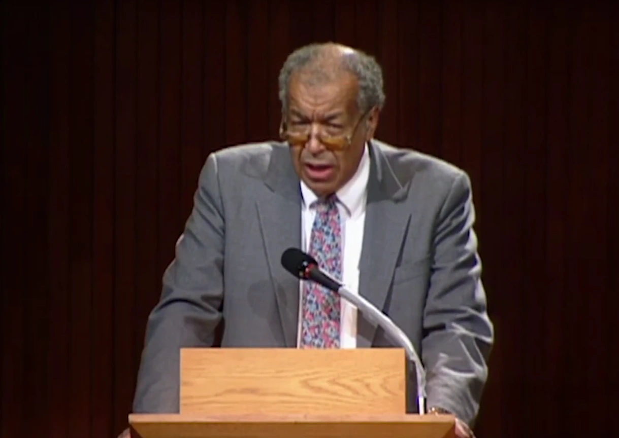 A. Leon Higginbotham speaking at a podium on stage, in front of a dark background