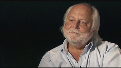 Man seated in front of a black background for an on camera interview.