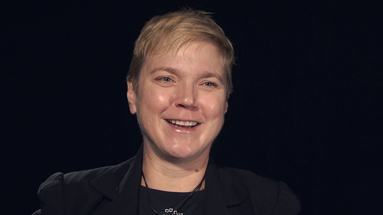 Linda Griffith seated in front of a black background for an on camera interview, smiling.