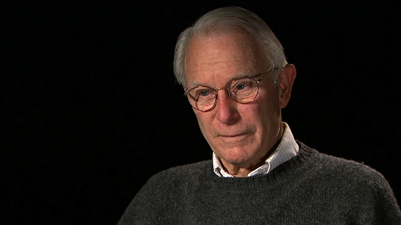 Donald L. M. Blackmer seated in front of a black background for an on camera interview.