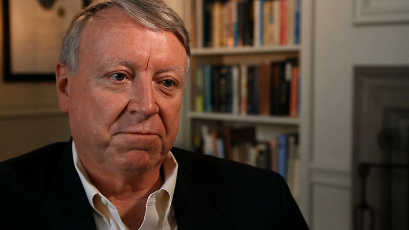 Edwin L. Thomas seated in room for an on camera interview, large white bookshelf in background.