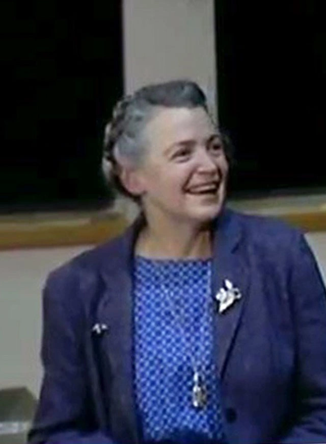 Mildred Dresselhaus stands in front of a chalkboard, looking to the side and speaking.