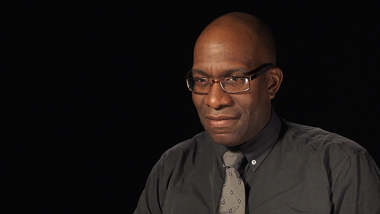 Lawrence Sass seated in front of a black background for an on camera interview.