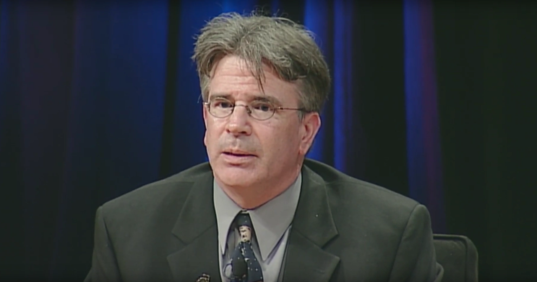 David W. Thompson speaking at podium on stage, blue curtain in background