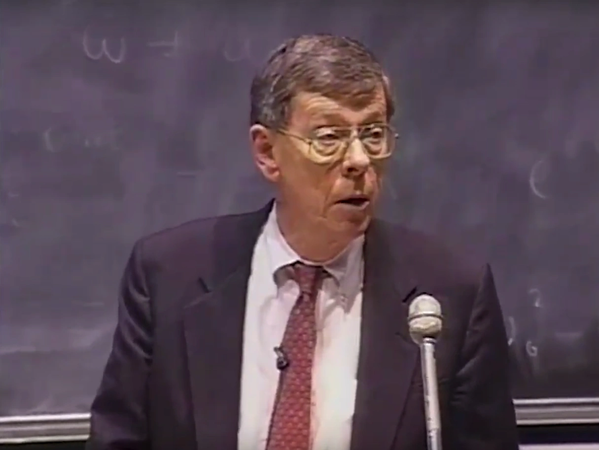 John A. Armstrong lecturing at a podium in a classroom, chalkboard in the background.