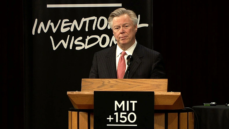Dean David Schmittleinspeaking at a podium on stage, in front of a dark background