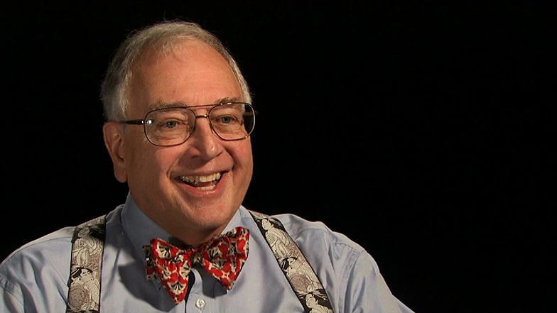 Bill Hetcht seated in front of a black background for an on camera interview, smiling.