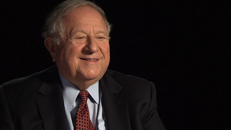 Edward Roberts sitting in front of a dark background for interview, smiling.