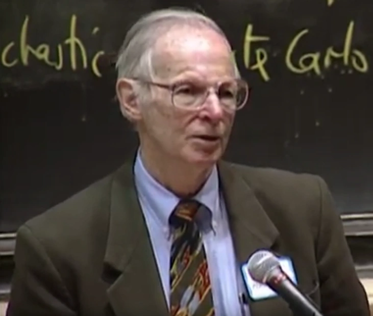 Paul MacCready speaks into a microphone in front of a chalkboard