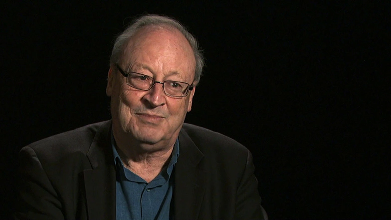 William J. Mitchell seated in front of a black background for an on camera interview, smiling