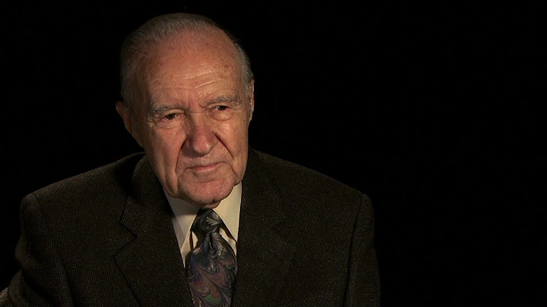 Gene M. Brown seated in front of a black background for an on camera interview.