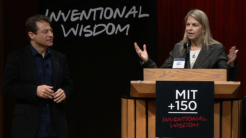 Dava Newman speaks onstage at a podium, black background behind her