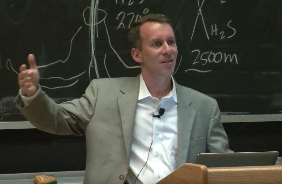 Bobby Braun lecturing at a podium in front of a chalkboard