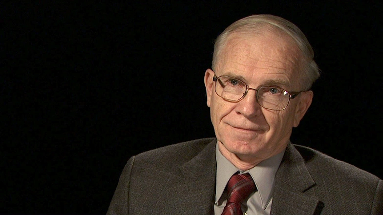 J. Kim Vandiver seated in front of a black background for an on camera interview.
