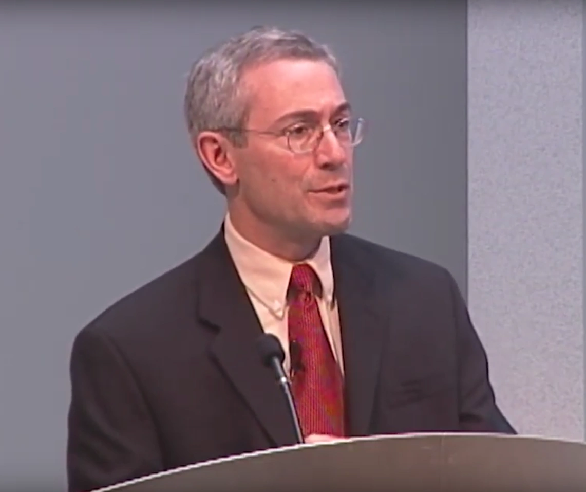 Tom Insel speaks at a podium, in front of a gray background