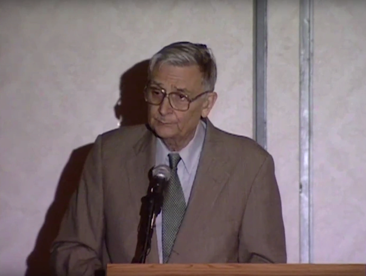 Edward O. Wilson speaking at a podium, cream colored wall in background